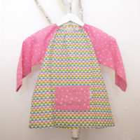 Bata para guardería, con estampado de triángulos y mangas y bolsillo delantero en rosa.